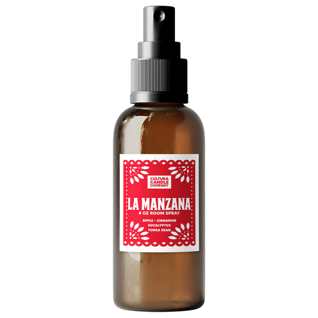 An amber glass room spray bottle with a black spray nozzle and a red and white paper label reading 'La Manzana 4 Oz Room Spray' by Cultura Candle Company, shown on a plain white background.