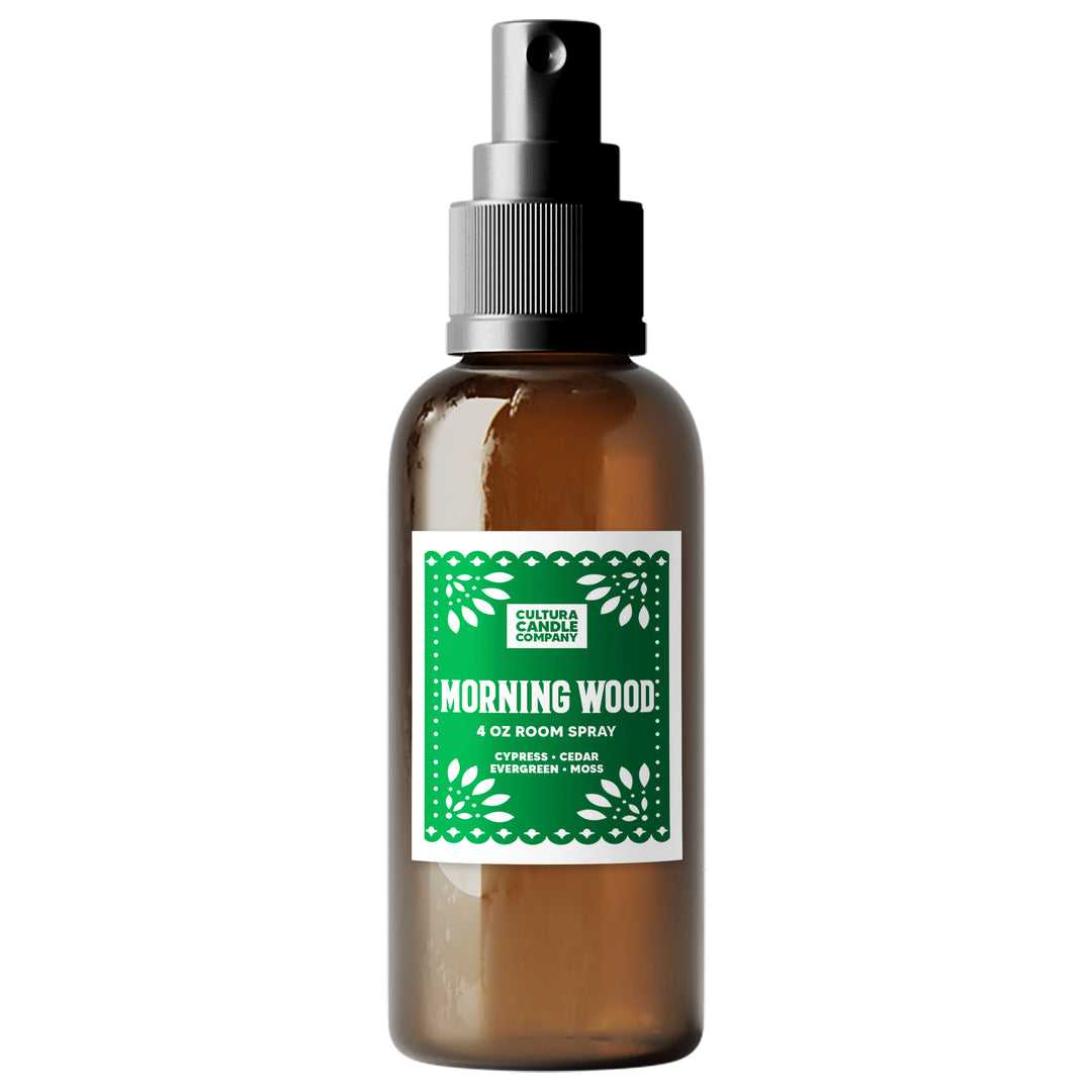 An amber glass room spray bottle with a black spray nozzle and a green and white paper label reading 'MORNING WOOD' by Cultura Candle Company, isolated on a white background.