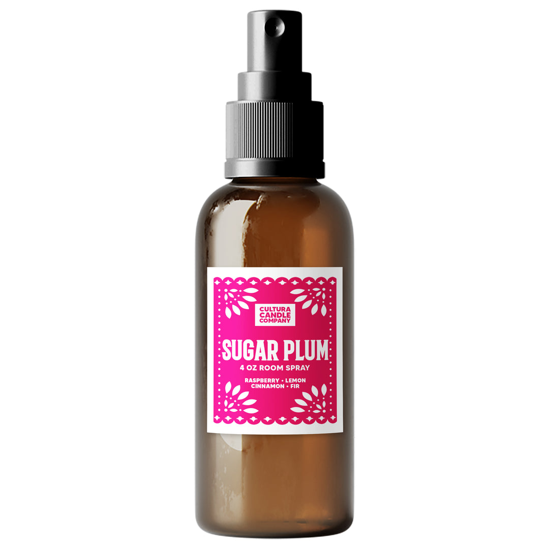 An amber glass room spray bottle with a black spray nozzle and a bright pink label reading 'SUGAR PLUM' by Cultura Candle Company, shown on a plain white background.