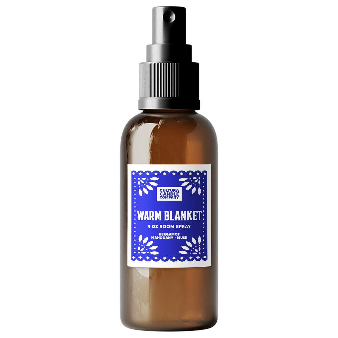 A 4 oz room spray bottle from Cultura Candle Company, featuring an amber glass bottle, a black spray nozzle, and a blue and white label that reads 'WARM BLANKET'.